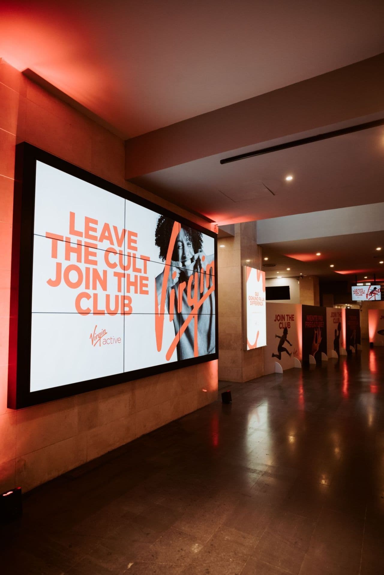Digital billboard displaying the Virgin Active "Leave the Cult Join the Club" campaign in a red-lit hallway.
