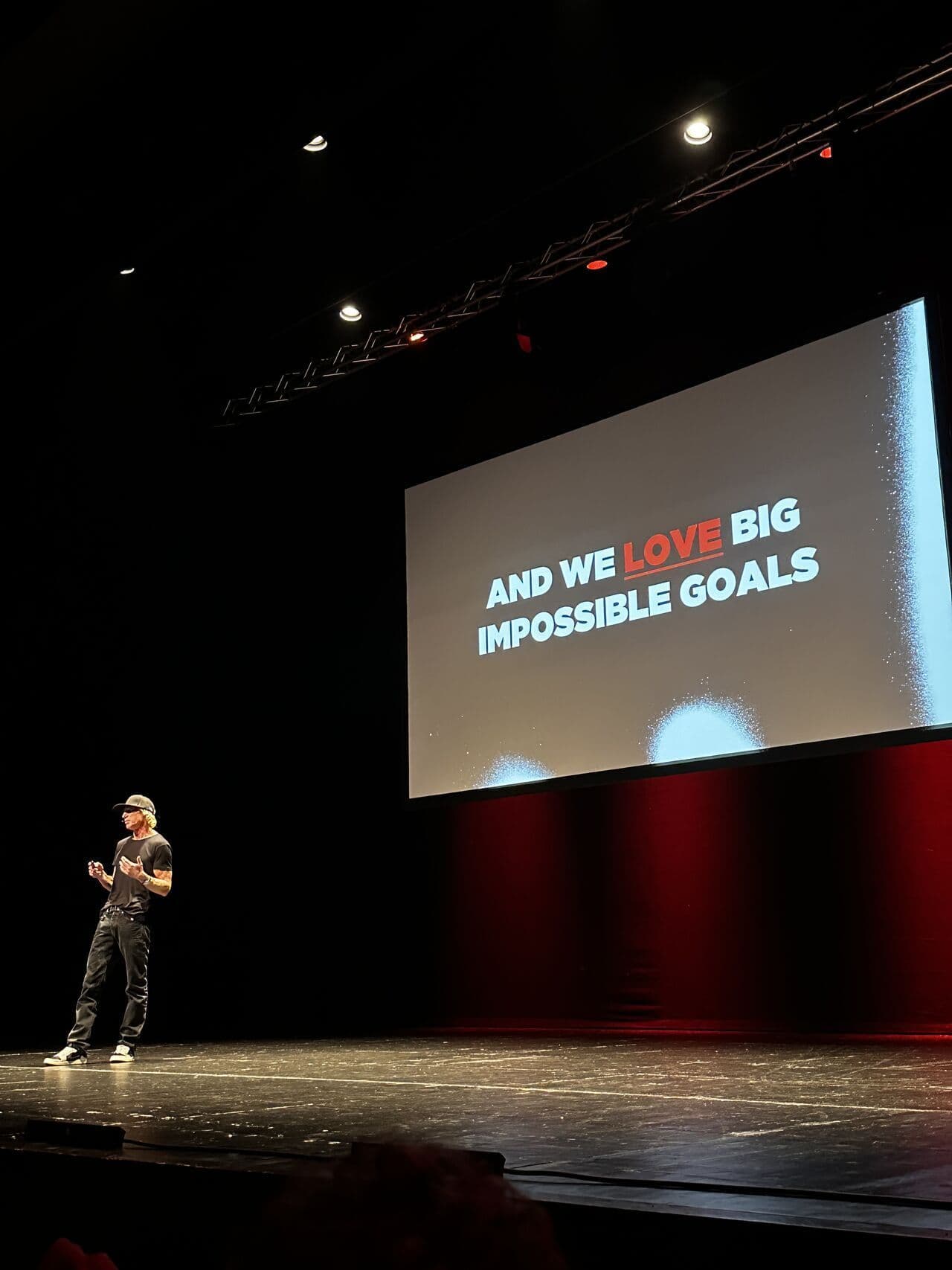Speaker on stage at a Virgin Active event with a screen displaying the text "And we love big impossible goals".