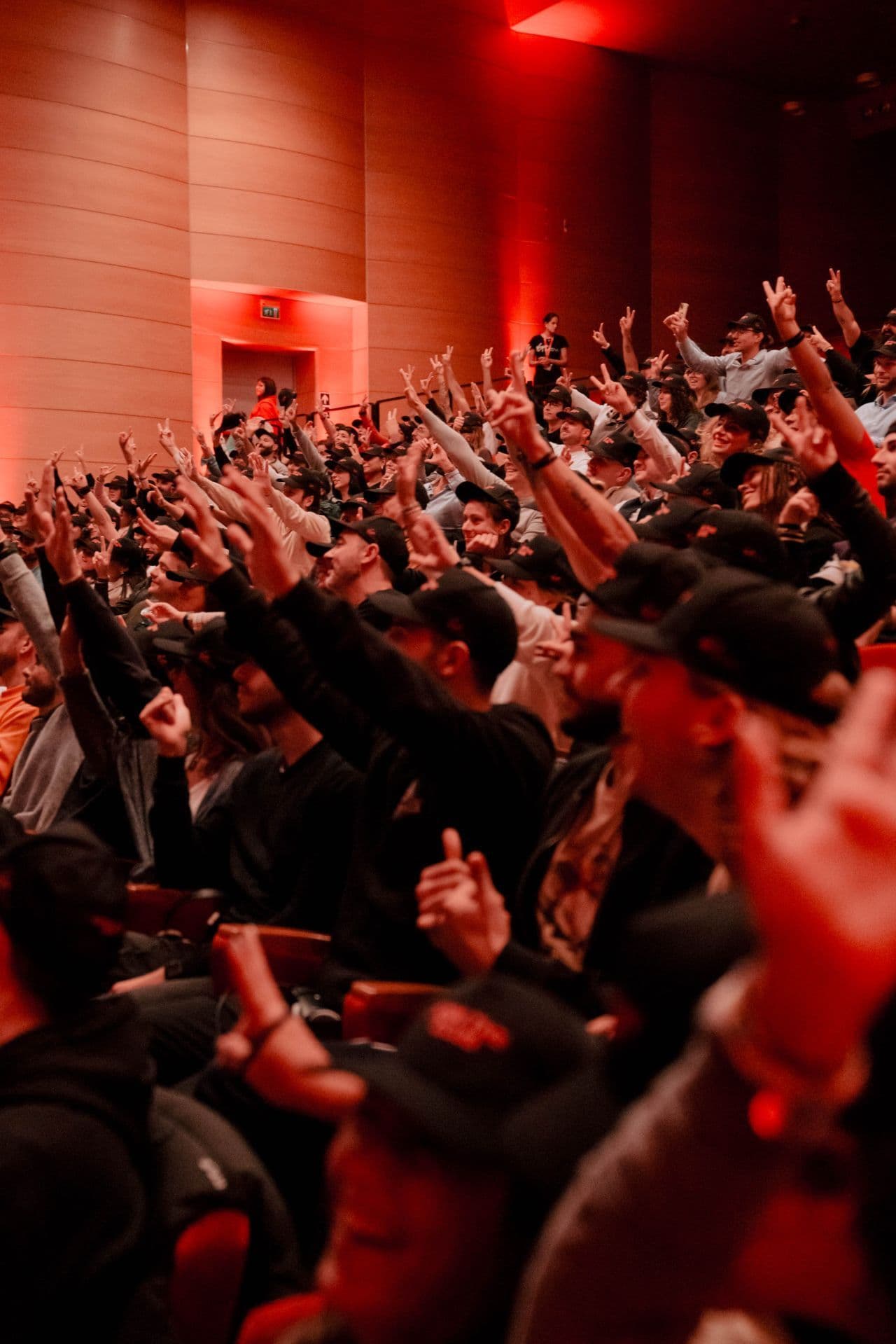 An engaged audience in a red-lit auditorium raising their hands and making peace signs during a Virgin Active event.