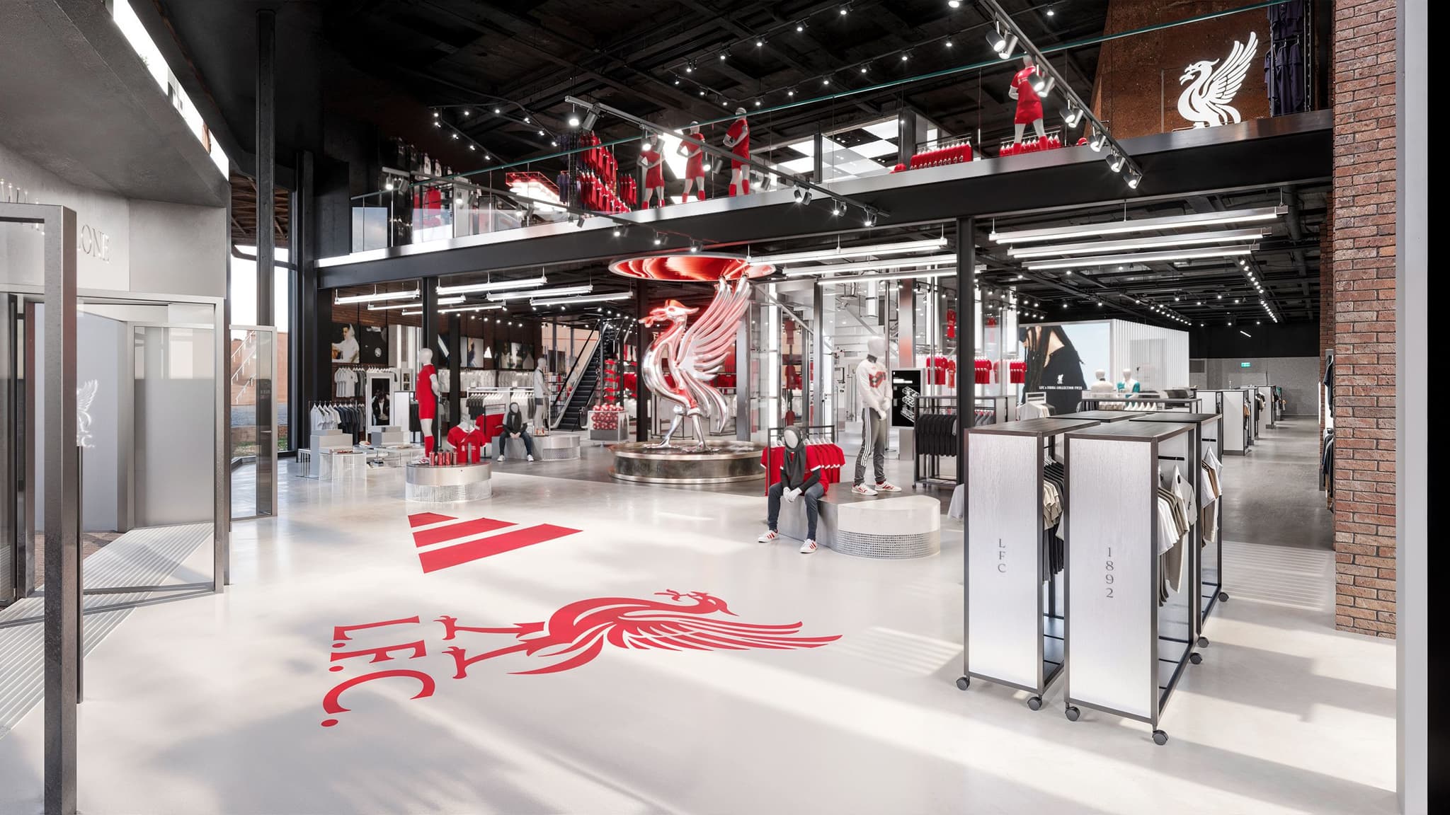Wide interior view of the Liverpool FC club store featuring a large floor crest, silver Liverbird statue, and two floors.