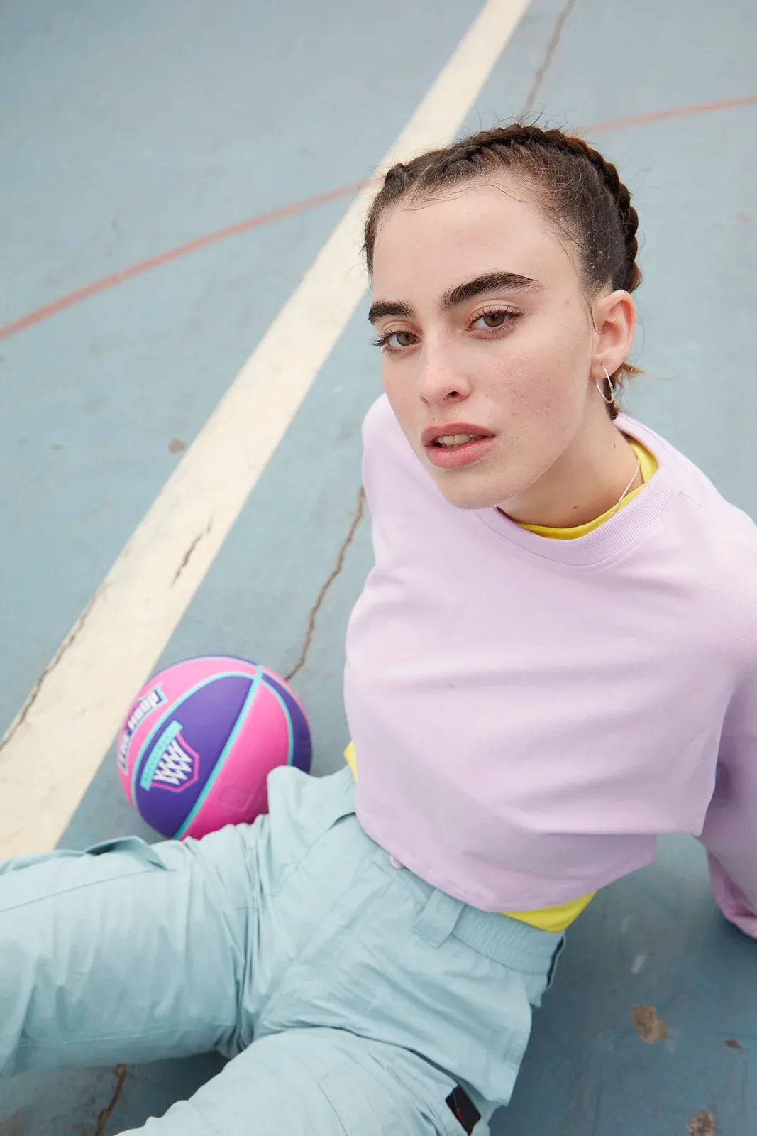 Young woman in a pink sweater sitting on a blue basketball court next to a colorful basketball.