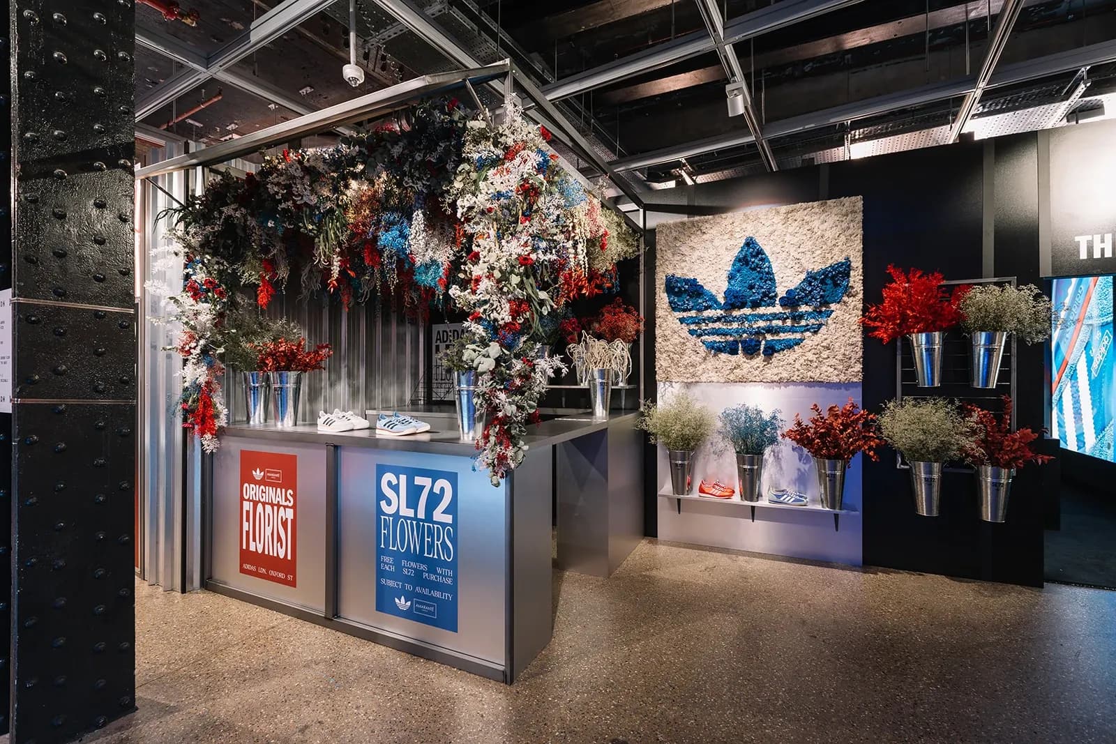 "Originals Florist" pop-up stand featuring a blue floral trefoil logo on the wall and buckets of dried flowers.