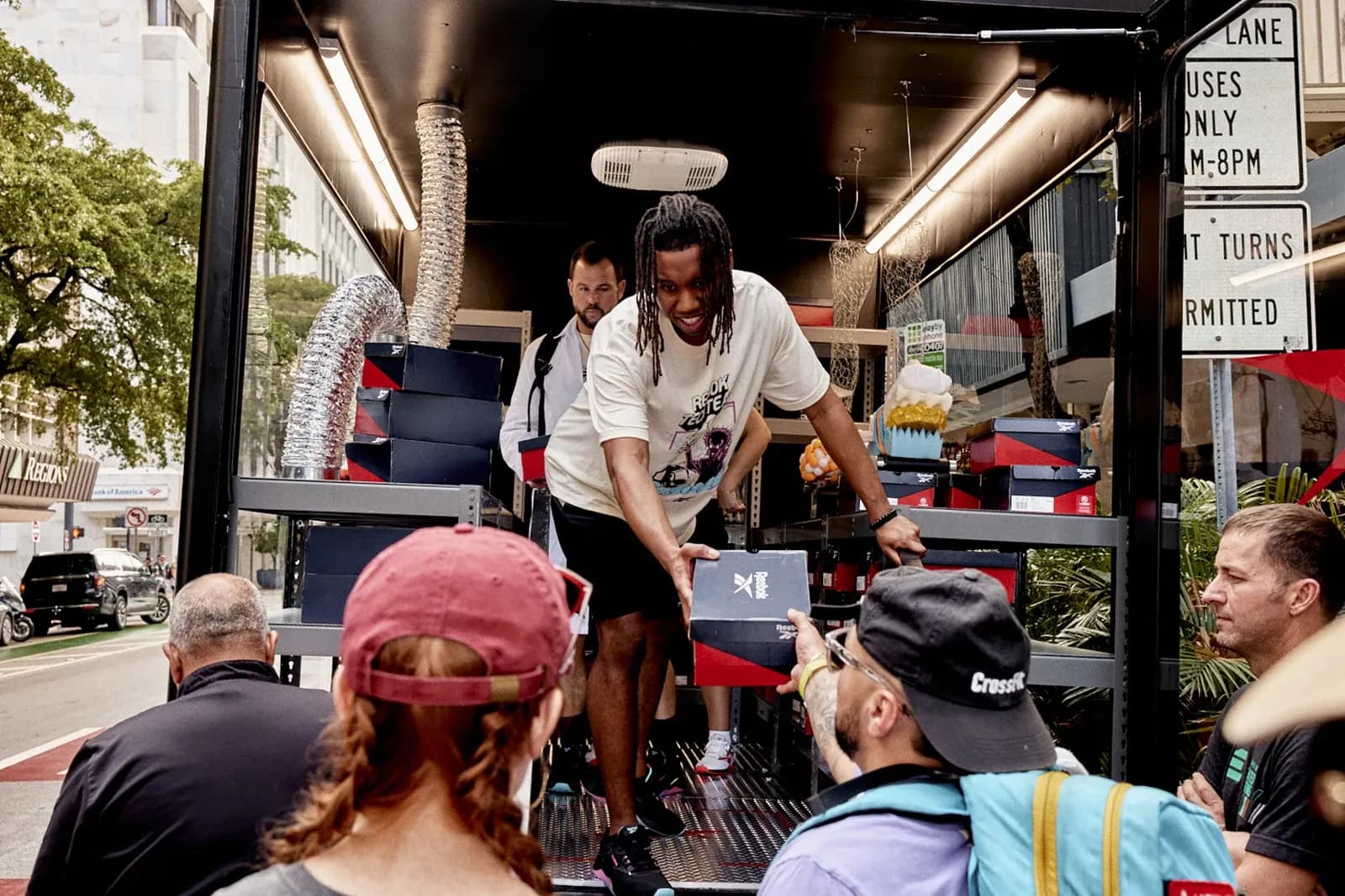 Staff member handing a Reebok shoe box to a person in a crowd from the back of a black activation truck.