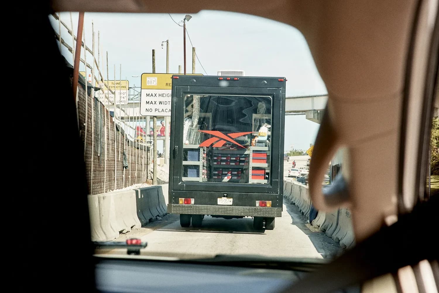 Rear view of a black Reebok delivery truck on a highway showing shelves of shoe boxes through the back window.