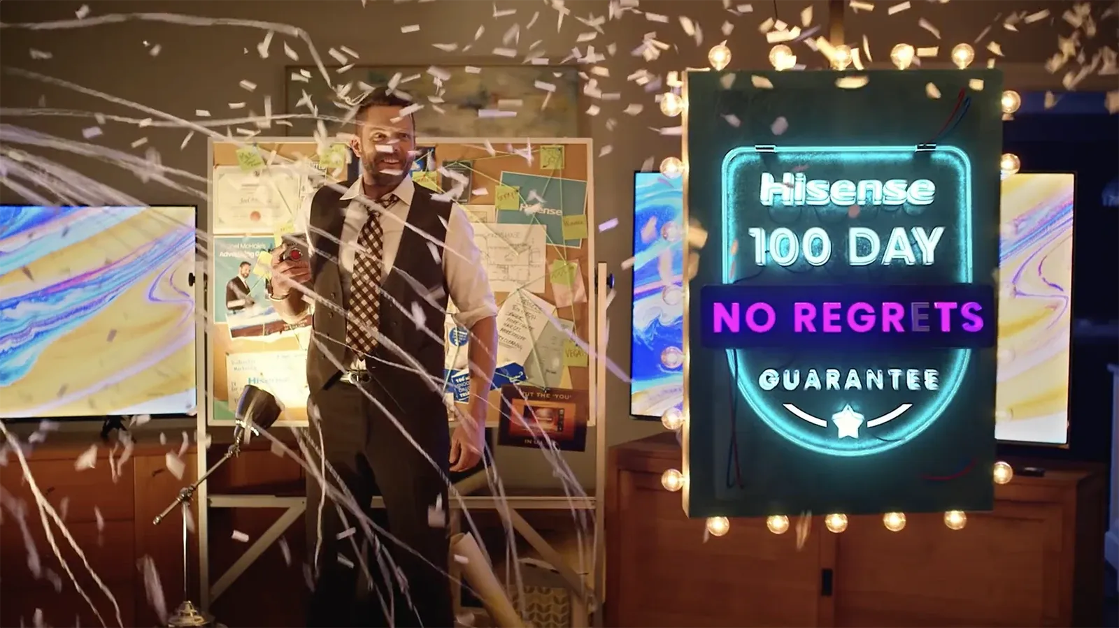 Man standing amidst falling confetti next to a lit neon sign for the "Hisense 100 Day No Regrets Guarantee".
