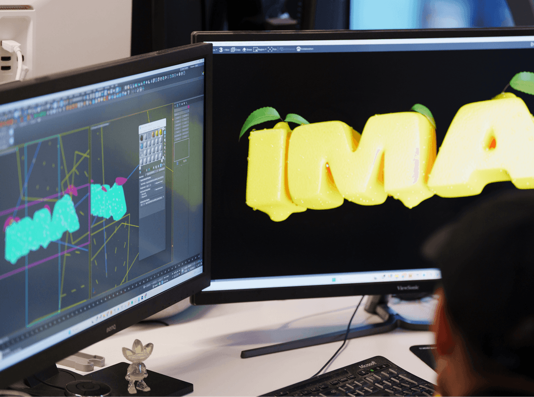 Close-up of dual computer monitors displaying graphic design and video editing software in a dark studio.