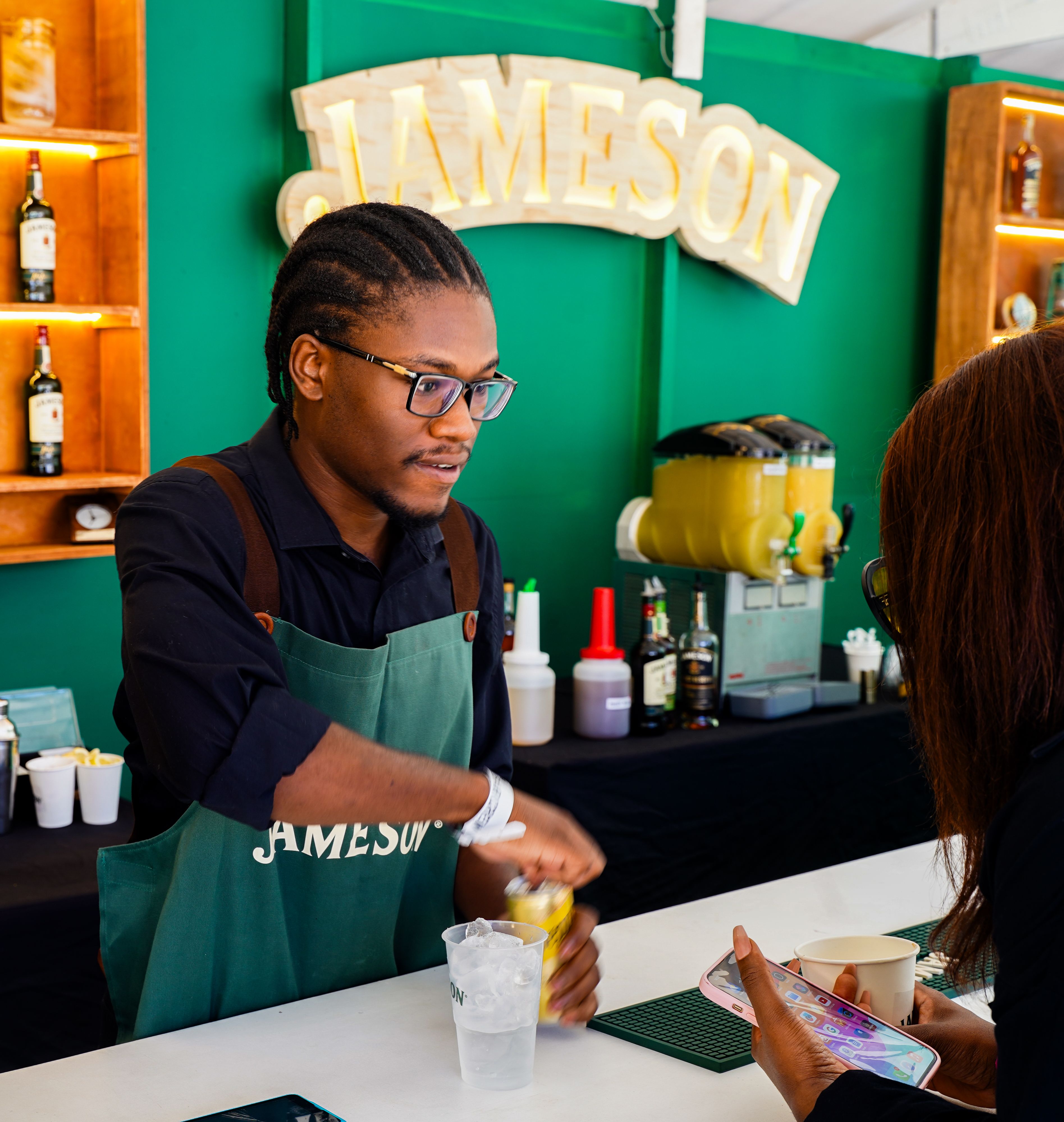 Bartender wearing a green Jameson apron serving a customer at a bright green branded event bar.
