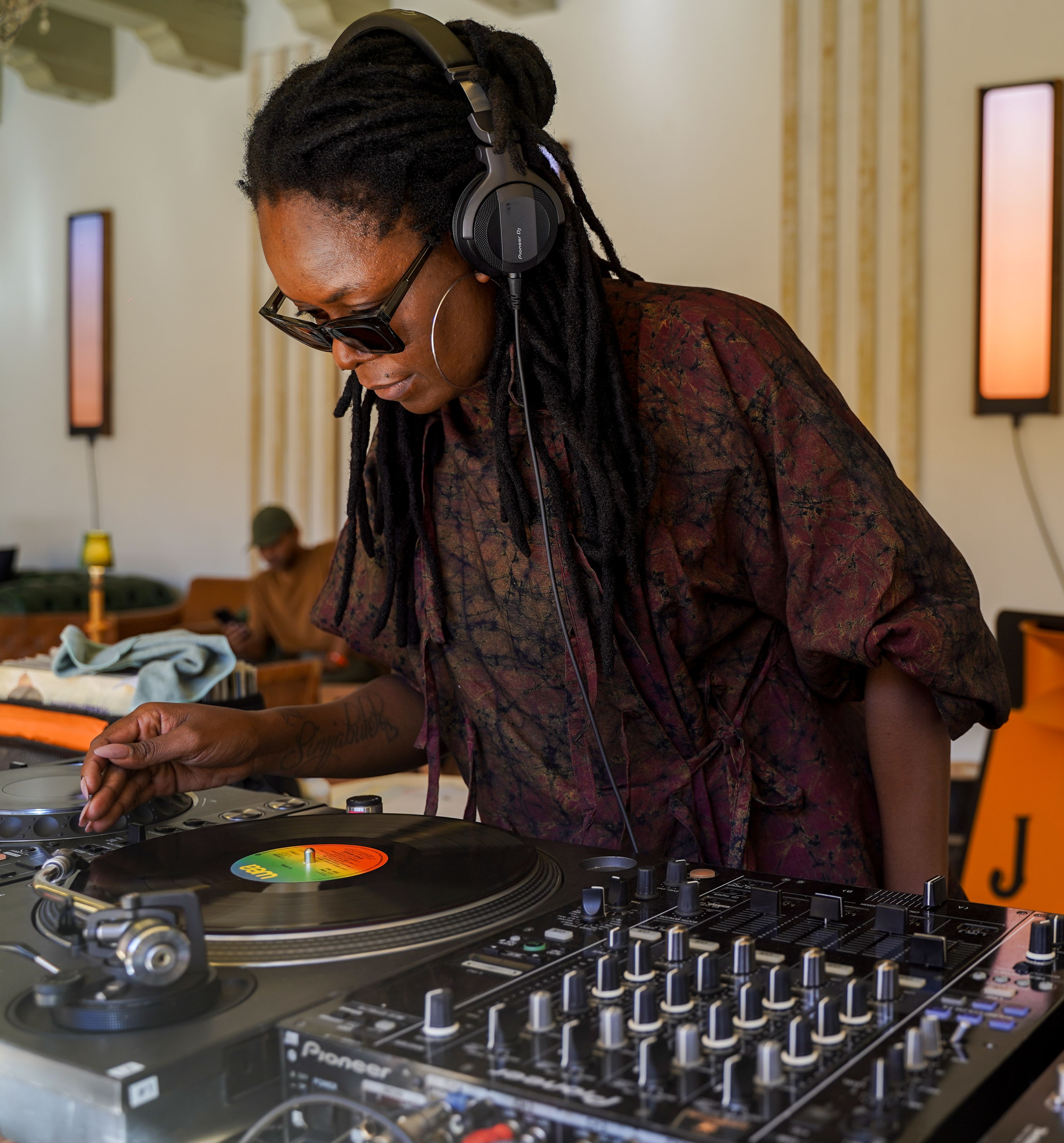 Female DJ with dreadlocks and sunglasses spinning vinyl records on Pioneer DJ turntables at a Jameson event.
