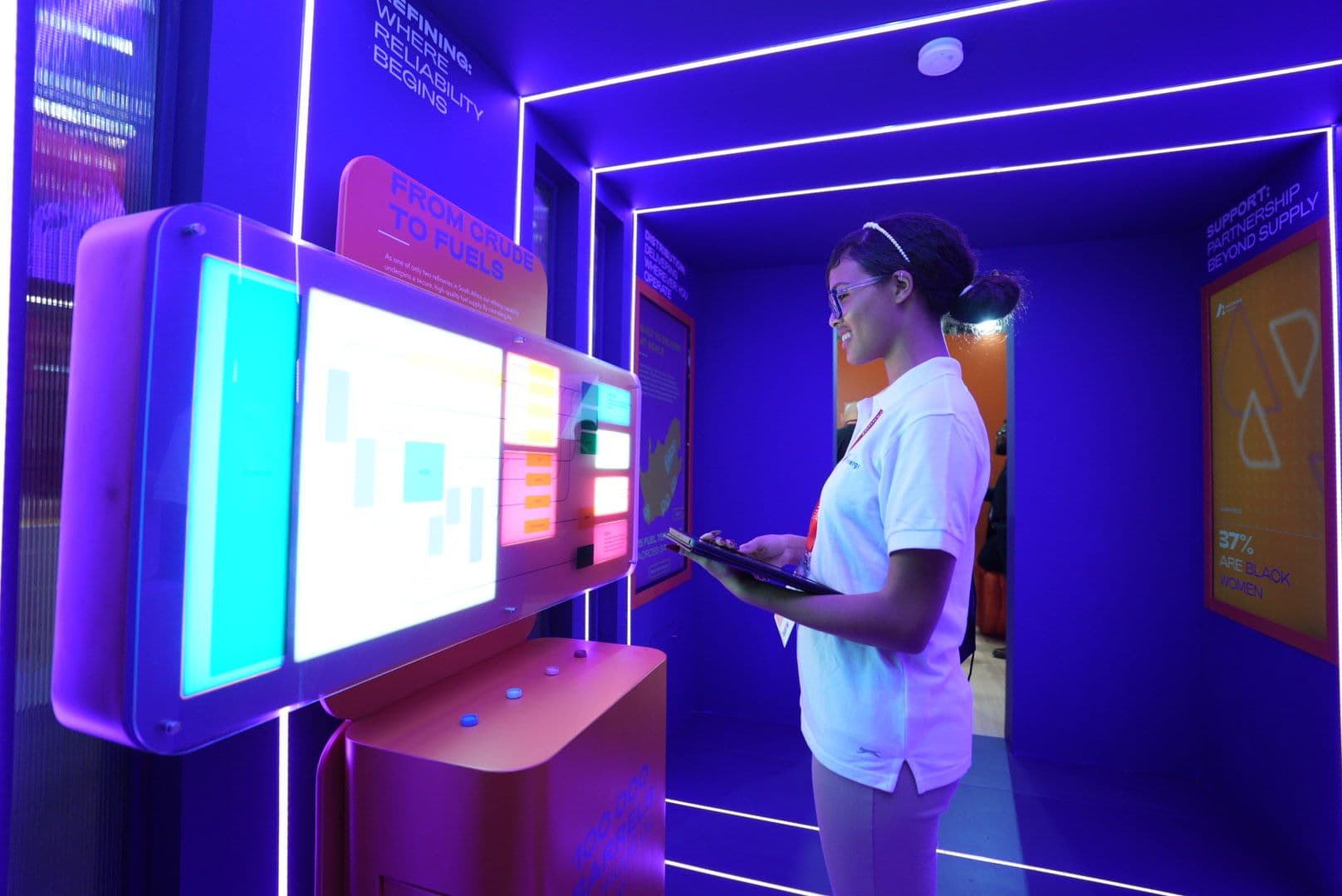 Woman interacting with a digital touch display inside the neon-lit purple tunnel of the Astron Energy exhibition stand.
