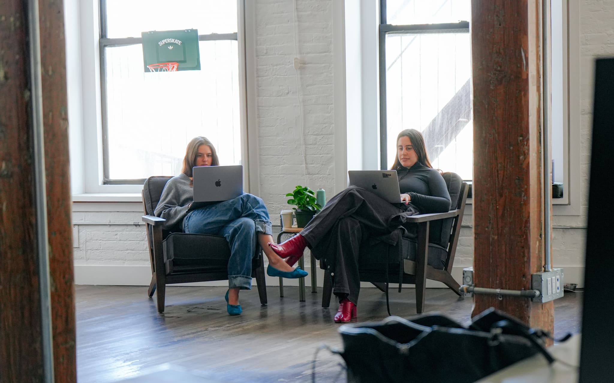 Two women working on laptops while seated in comfortable armchairs at the IMA New York office.