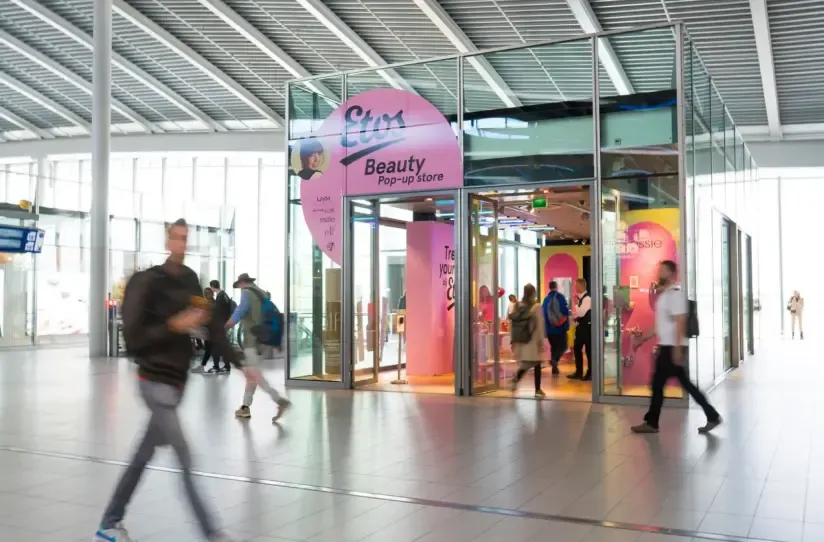 Exterior view of the glass-walled Etos Beauty Pop-up store located in a busy train station concourse.