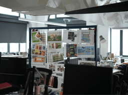 A printed IMA brand brochure resting on a wooden surface with a blurred green plant in the foreground.