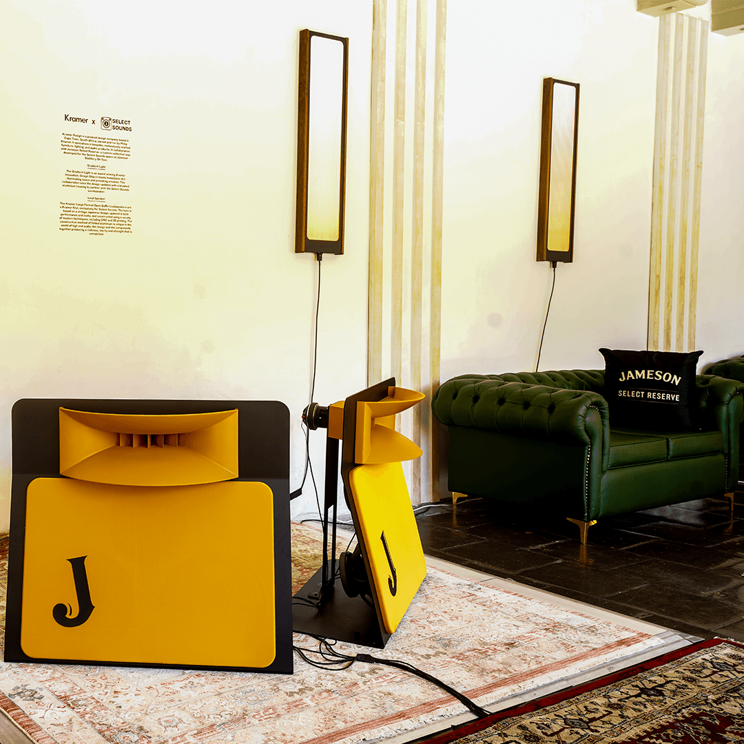 Jameson event lounge featuring a green leather sofa, branded pillow, and custom yellow acoustic speakers on a rug.
