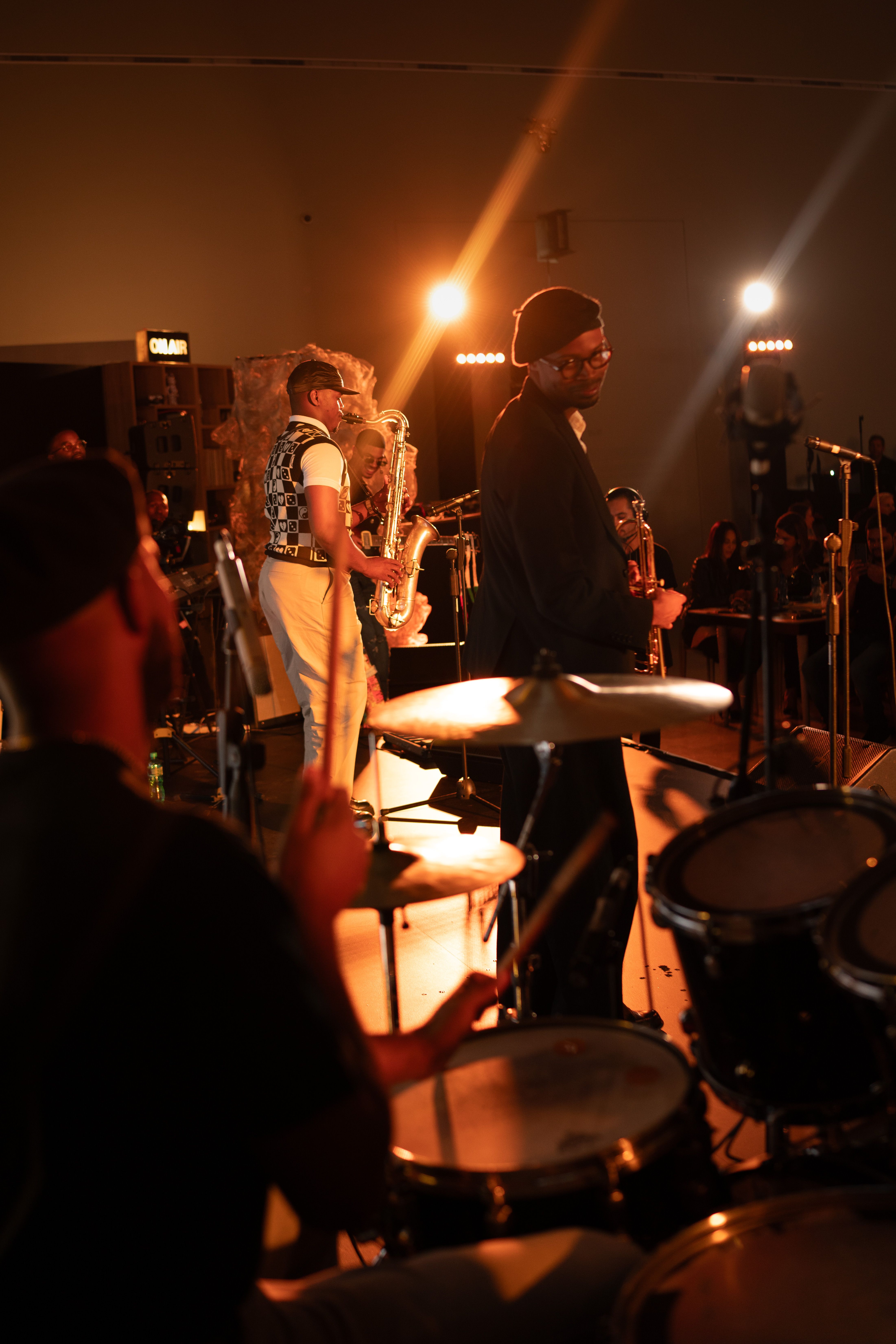 Live band performing on stage with a saxophone player in focus under warm orange concert lighting.