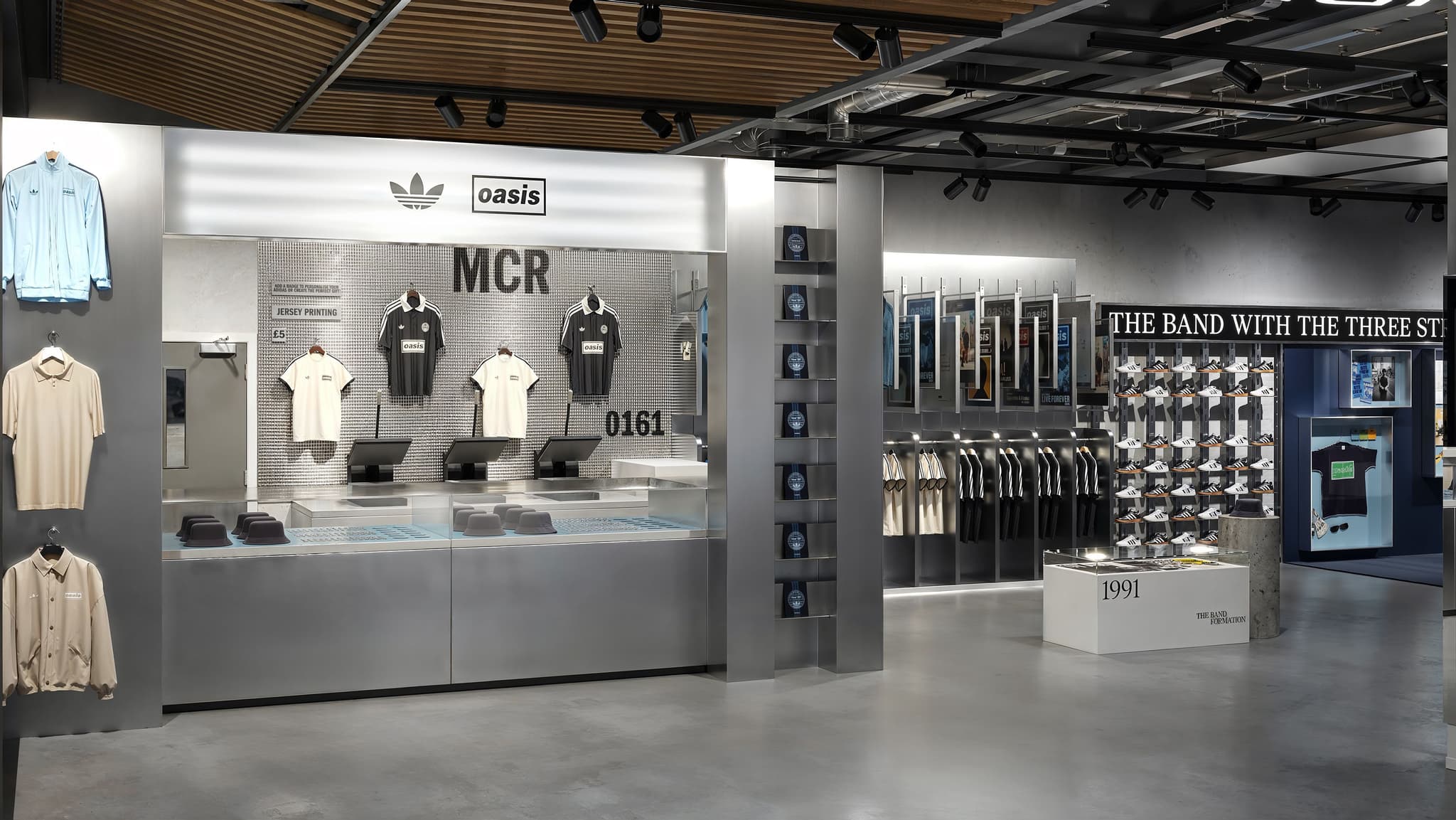 Adidas and Oasis jersey printing station in a retail store featuring MCR and 0161 text on a tiled wall display.