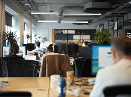 Employees working at rows of desks in a spacious, sunlit open-plan office in Manchester.