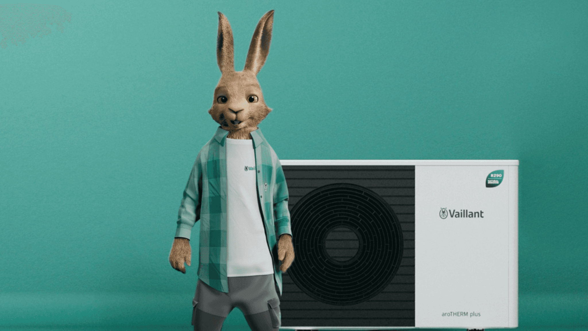 CGI hare mascot in a green checked shirt standing next to a Vaillant aroTHERM plus heat pump against a green background.