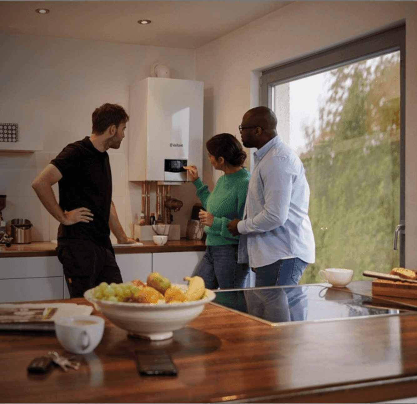 Heating engineer explaining a wall-mounted Vaillant boiler's digital display to a couple in their modern kitchen.