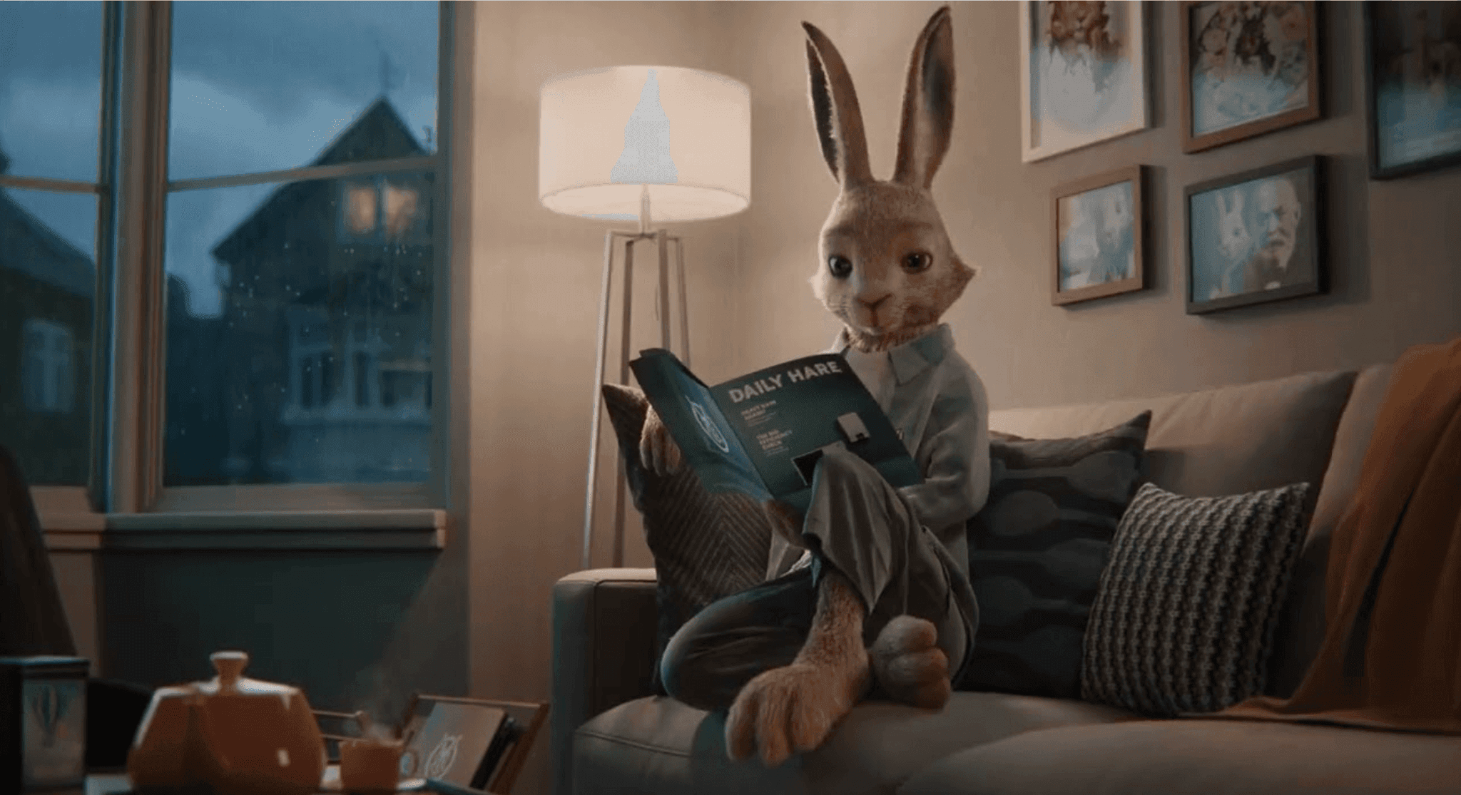 Vaillant hare mascot sitting on a grey living room sofa reading a green Daily Hare booklet.
