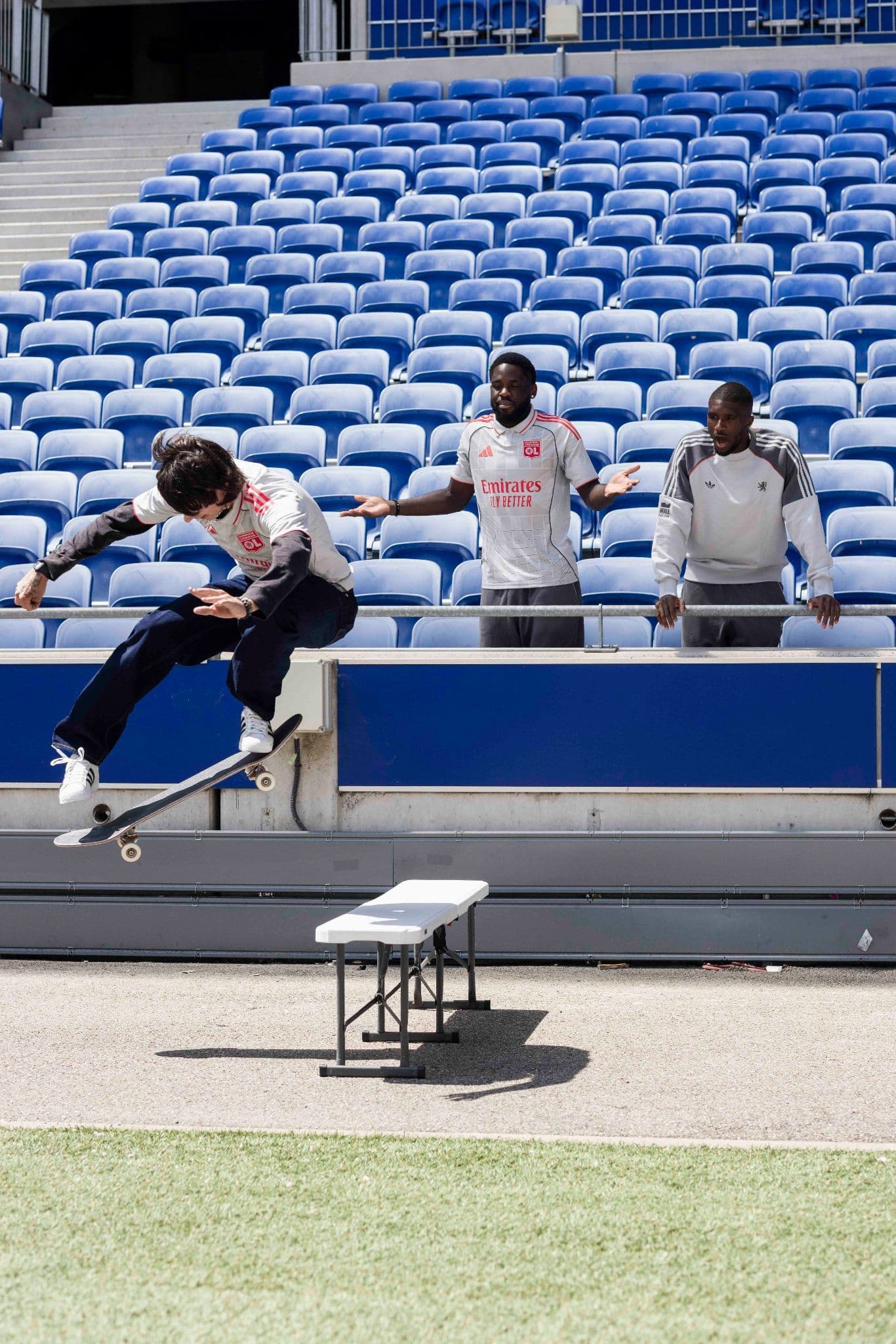 Person performing a skateboarding trick on a bench in front of blue stadium seats.