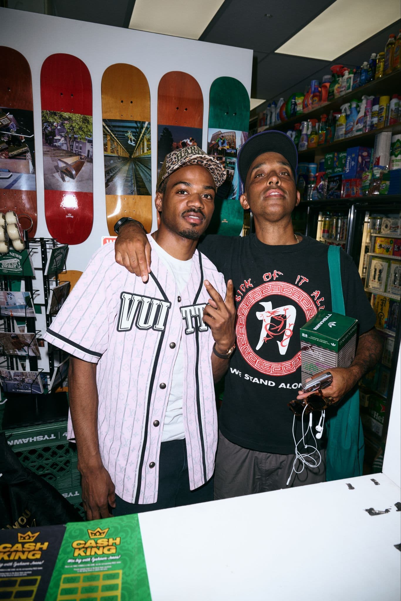 Two men posing for a photo inside a room with colorful posters in the background.