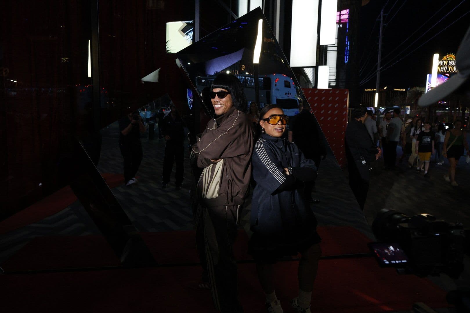 Two people standing outdoors at night near event signage and structures.