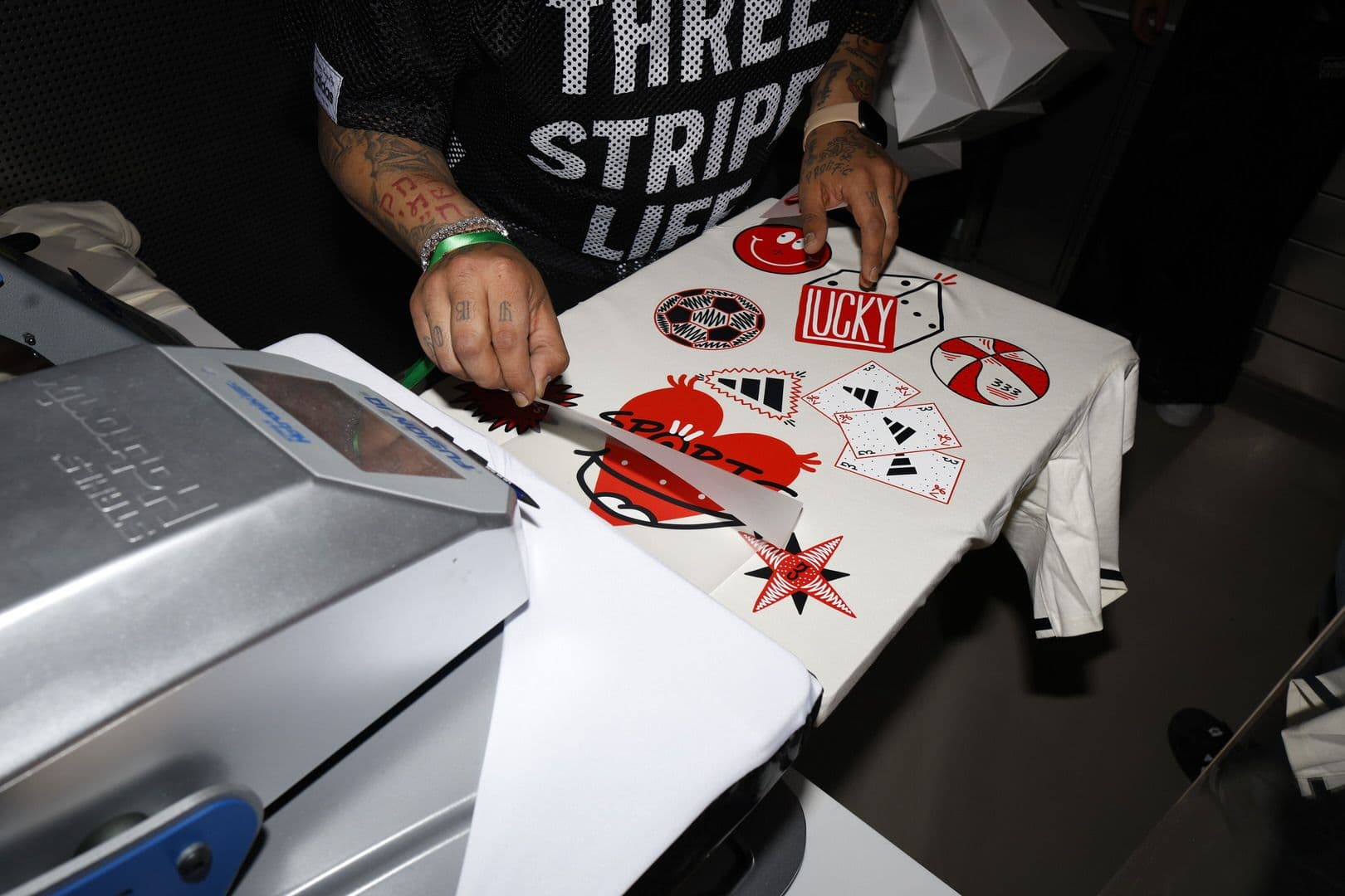 Close-up of a person in a "Three Stripes" shirt at printing station.