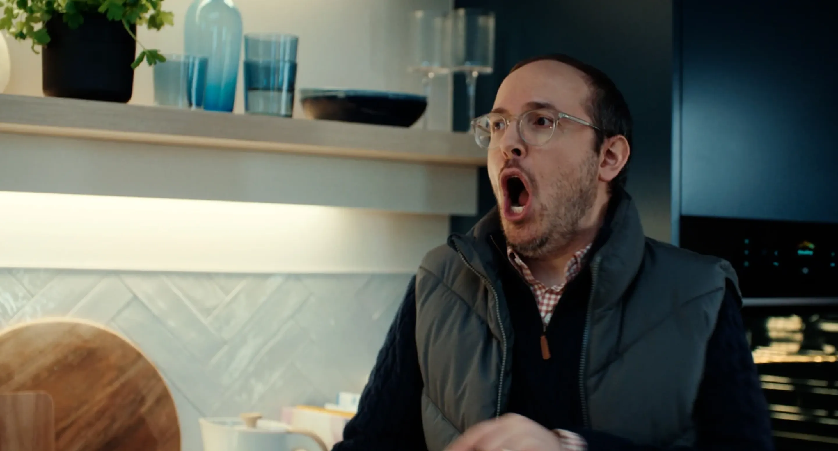 Close-up of a man with glasses looking shocked and amazed in a kitchen setting from a Hisense commercial.