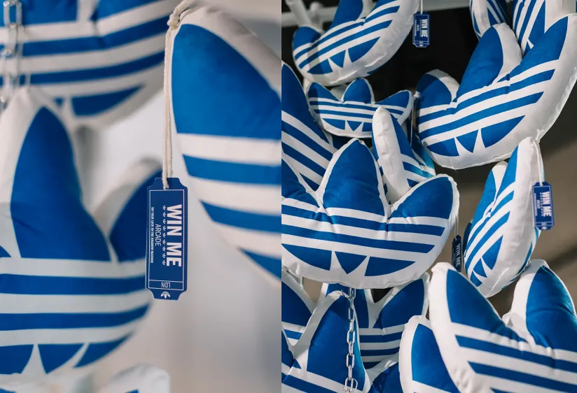 Close-up of blue and white plush Adidas trefoil logo toys hanging on chains with "Win Me" tags.