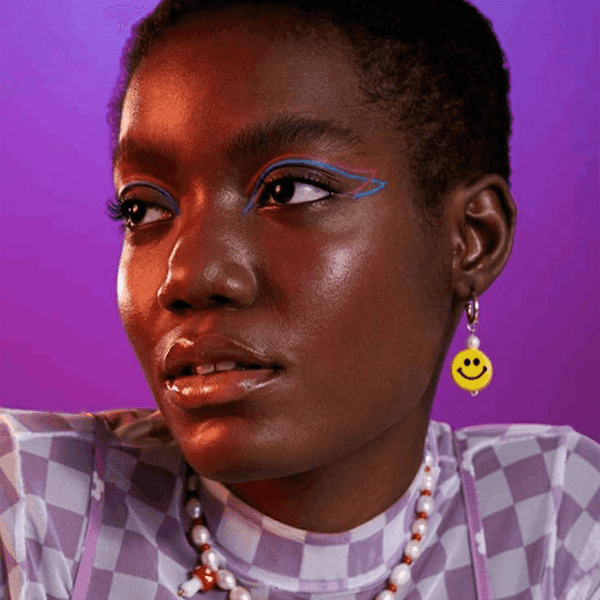 Close-up of a person with colorful eye makeup and a patterned shirt against a purple backdrop.