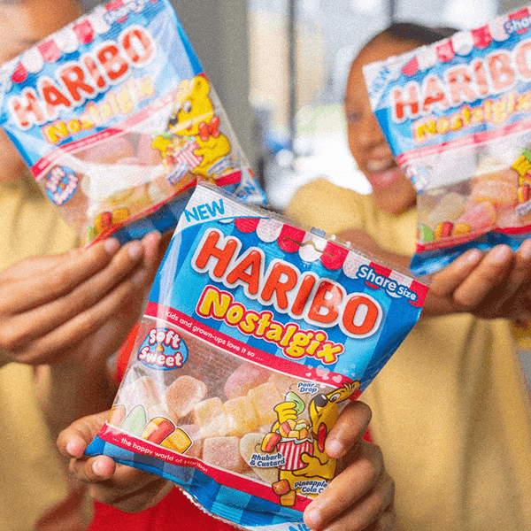 Two people holding bags of Haribo Nostalgia candy against an outdoor background.