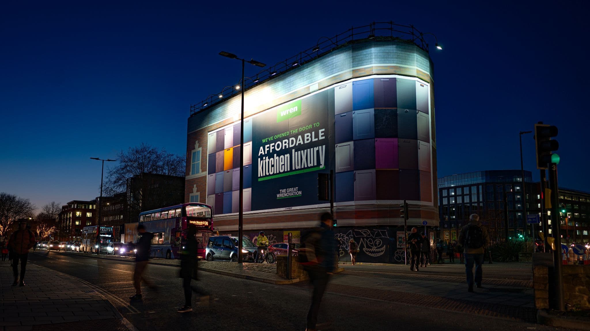 Illuminated building billboard displaying colorful cabinet doors and "Affordable kitchen luxury" text.