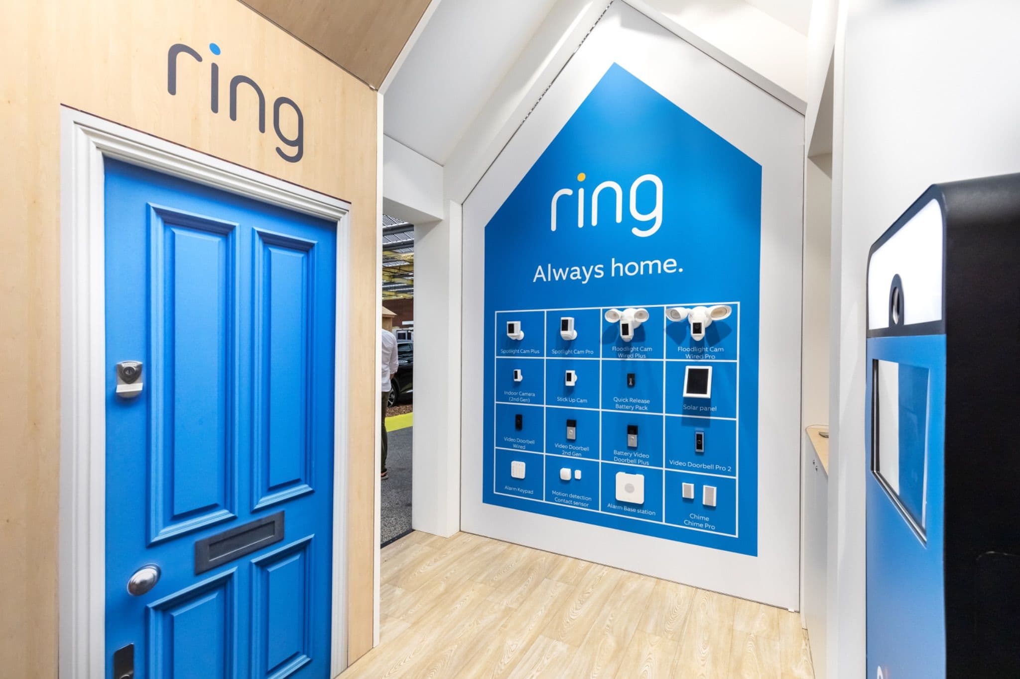 A mock front door setup adjacent to a grid display of Ring smart home security devices and accessories.