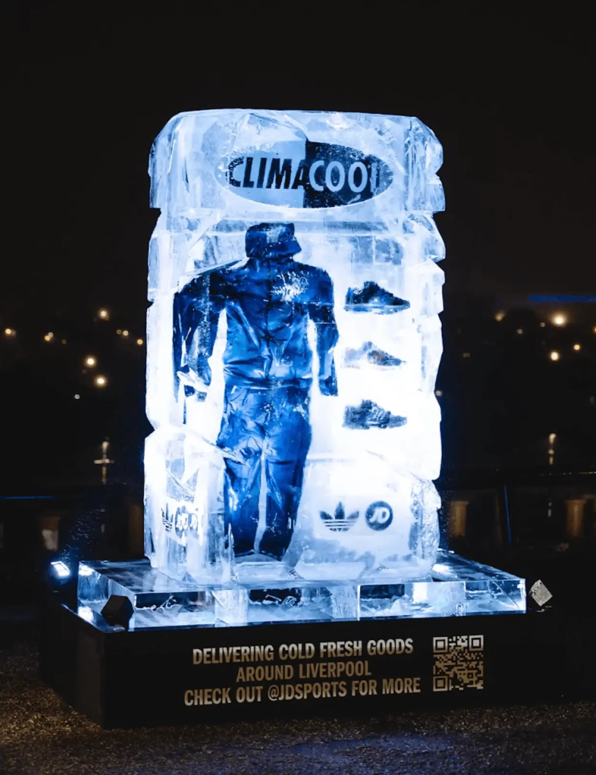 Lit ice sculpture displaying frozen Adidas Climacool clothing and shoes with JD Sports branding at night.