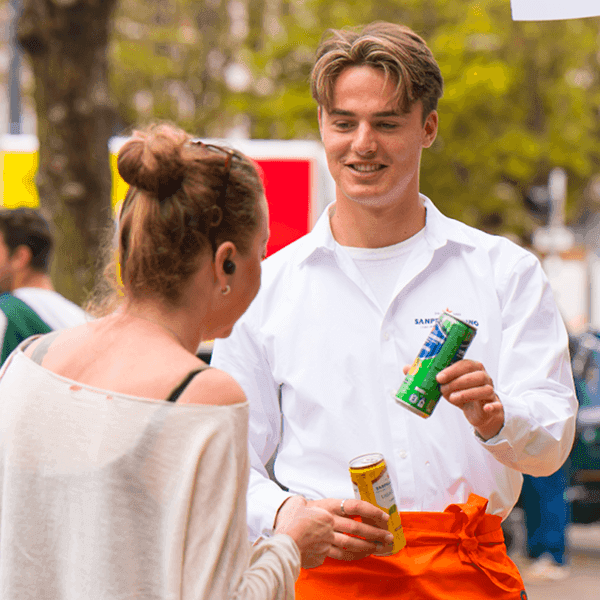Brand ambassador handing a San Pellegrino beverage to a customer at an outdoor promotional event.
