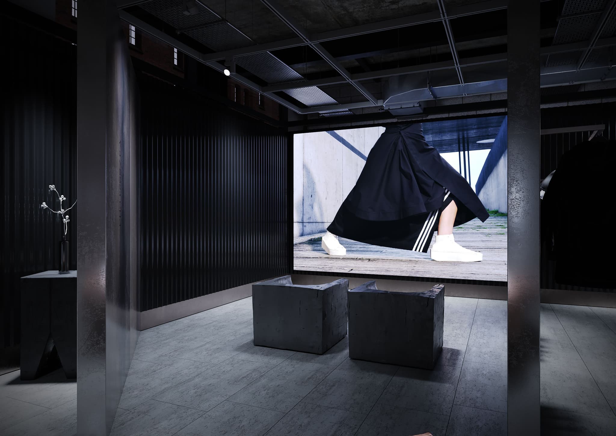 Large video display screen showing a fashion model in a Y-3 retail store, viewed from two brutalist block chairs.