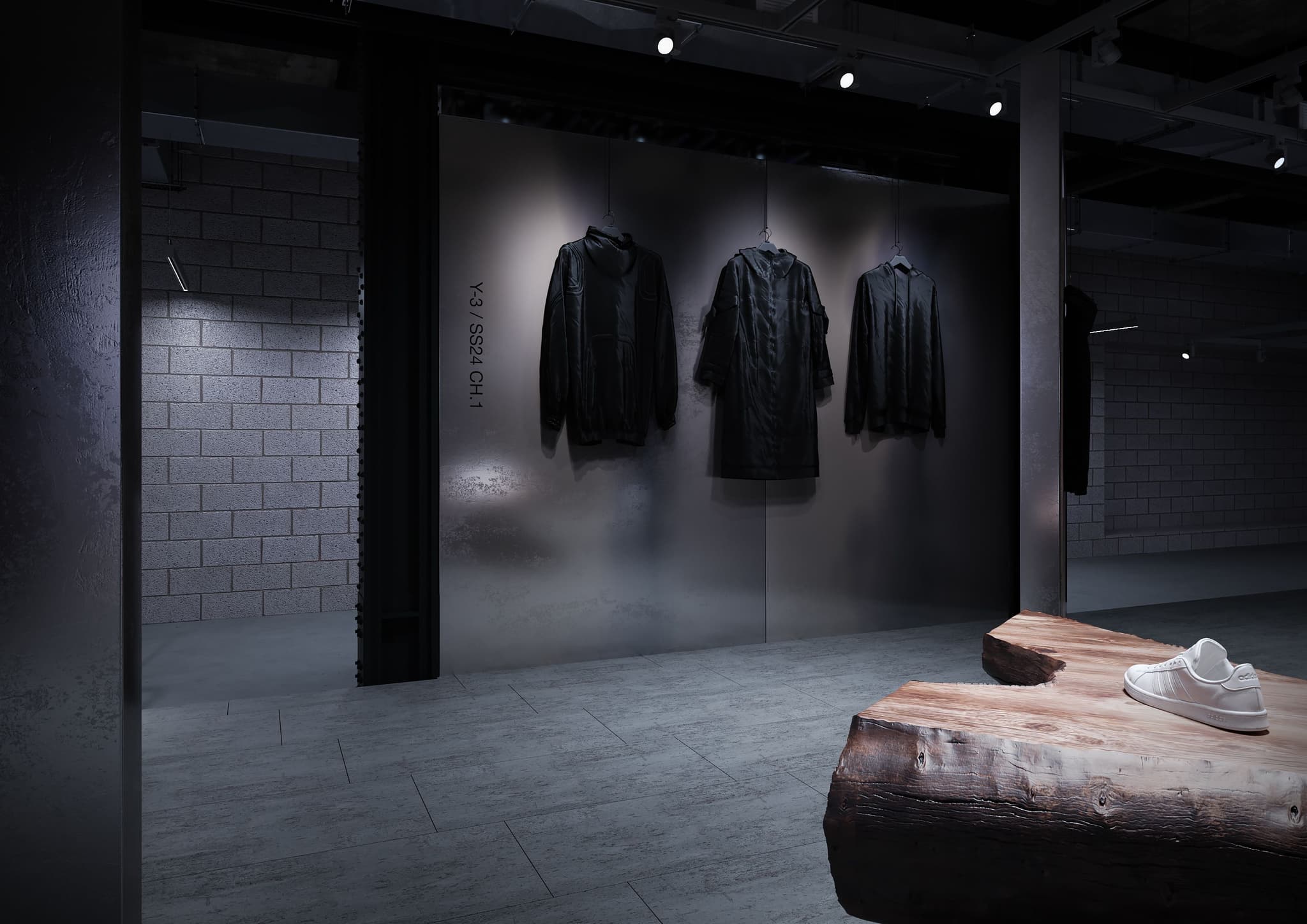 Black Y-3 apparel hanging on a steel wall display inside a minimalist store, next to a wooden table with a sneaker.