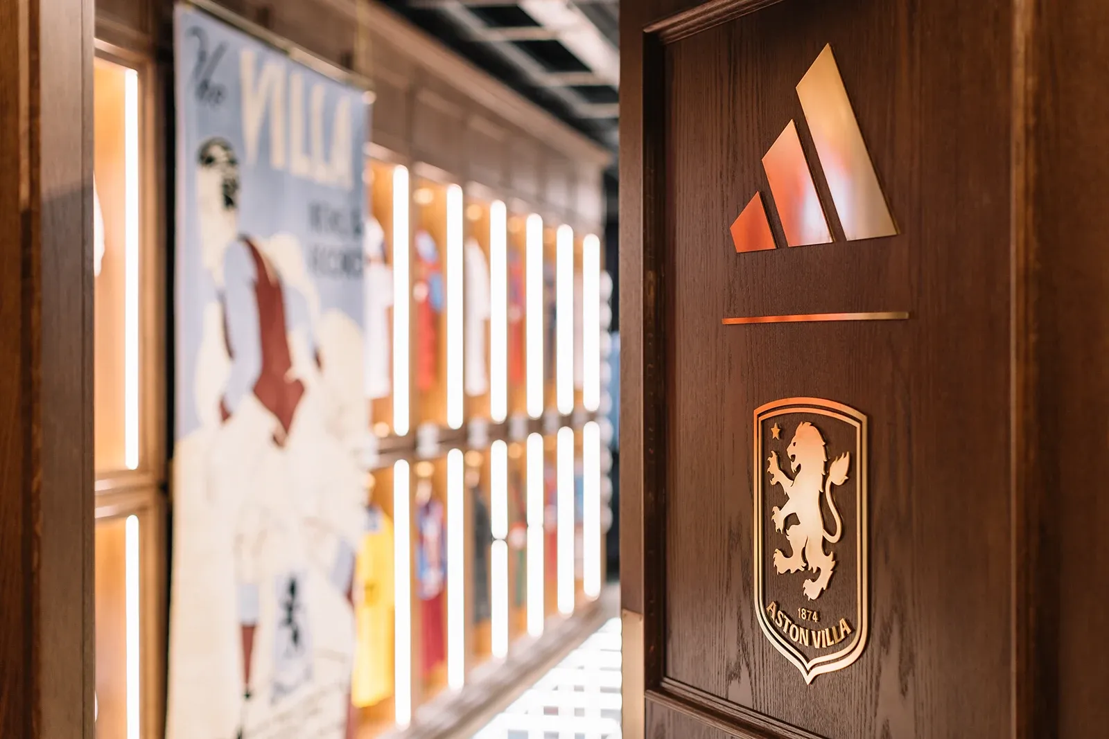 Close-up of a dark wooden door featuring gold relief logos of Adidas and the Aston Villa crest.