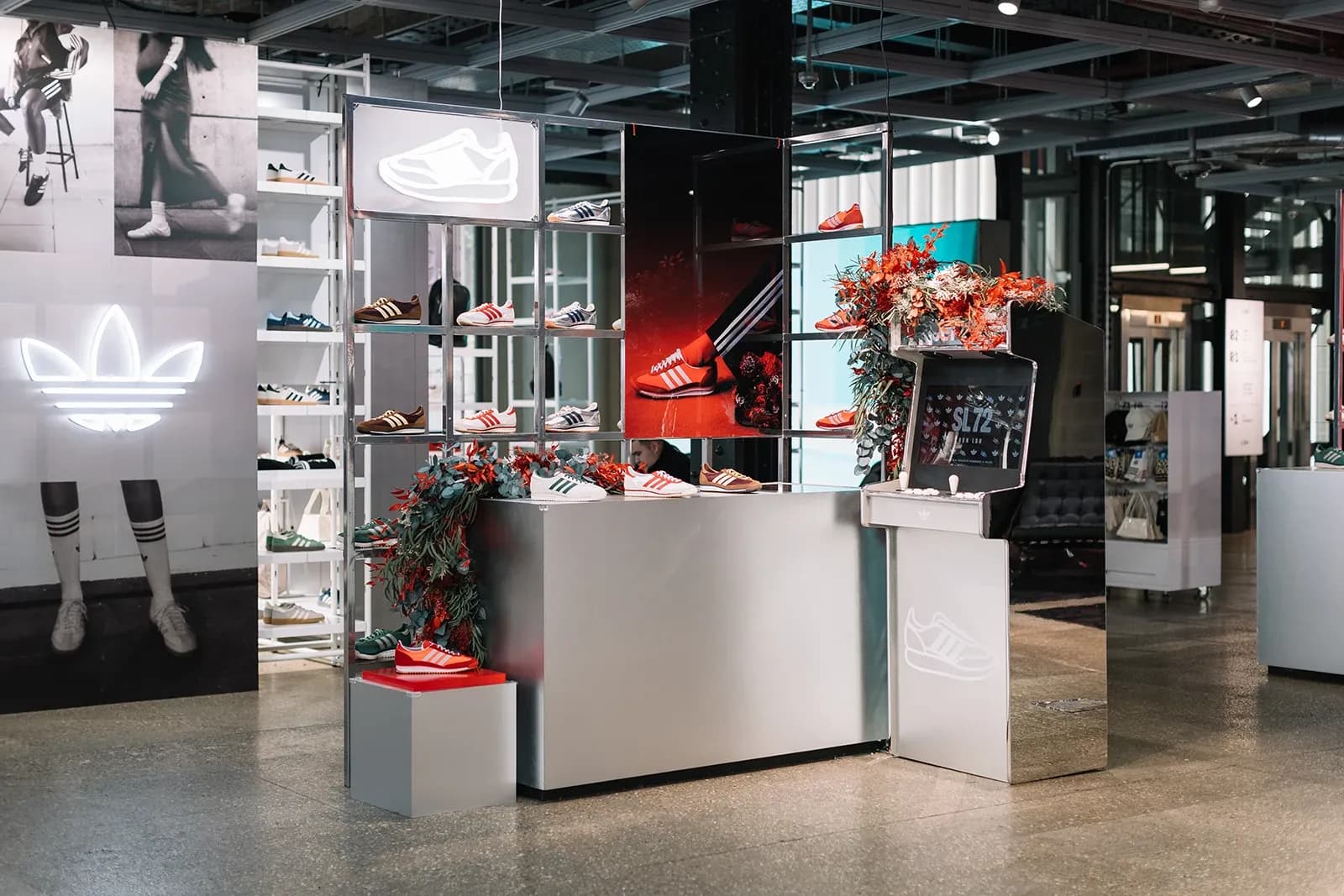 Chrome arcade machine branded with SL 72 and decorated with flowers on a silver counter in an Adidas store.