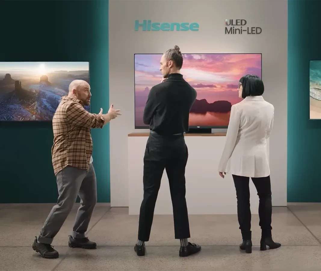 Three people discussing features in front of a large wall-mounted Hisense ULED Mini-LED TV display.