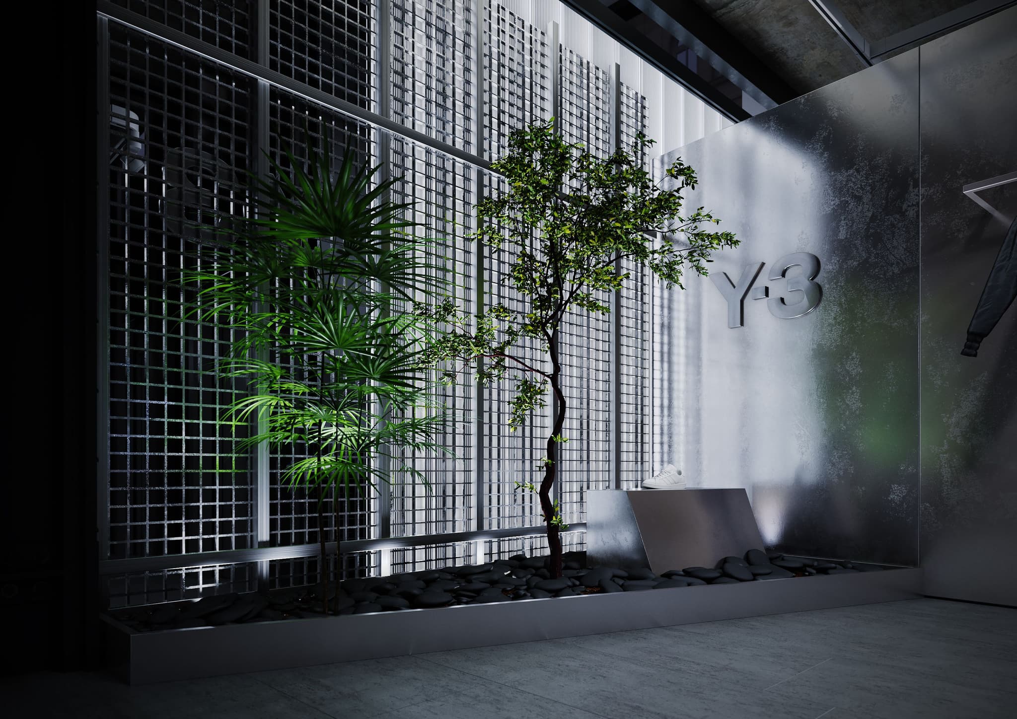 Green plants in a black rock bed next to a silver Y-3 logo and a white sneaker inside a minimalist industrial store.