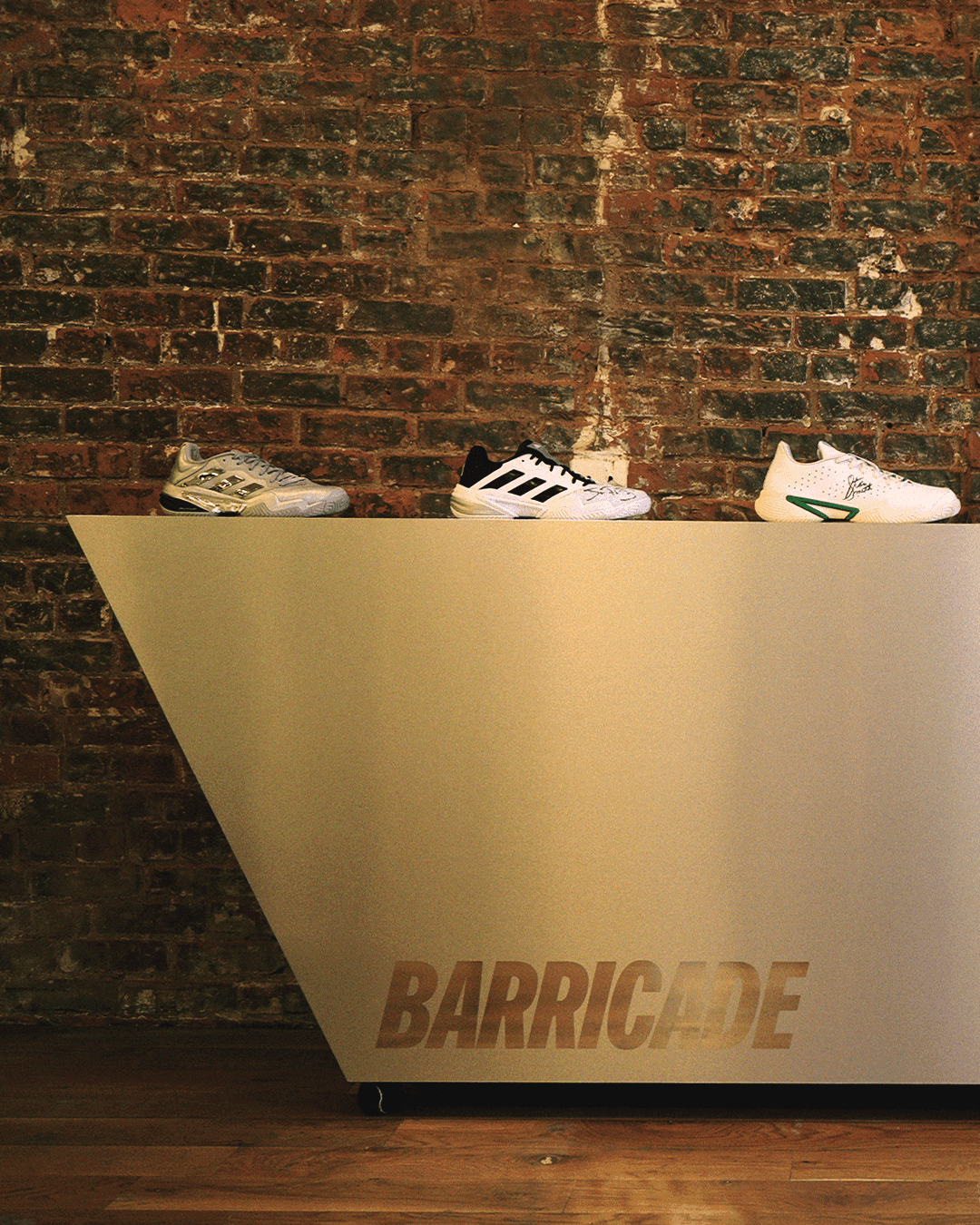 Three pairs of white adidas Barricade sneakers displayed on a sleek metallic podium.